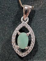 Front view of silver pendant with oval green stone and CZ halo