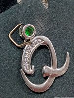 Front view of stylized silver-tone pendant with green stone, clear accents, yellow-tone bail