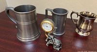 Three pewter vessels and elephant clock grouped on table