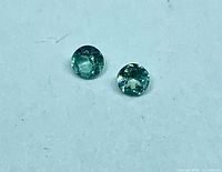 Pair of 3 mm round green alexandrite stones on white background