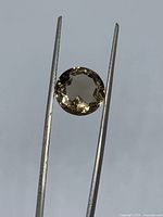 Round faceted smoky quartz held in tweezers front view