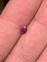 Oval ruby gemstone held between fingertips front view
