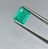 Front view of emerald-cut bluish green emerald held by tweezers