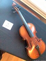 Full view of violin front showing body, fingerboard, tailpiece, chinrest; lot reference card visible