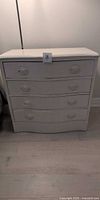Front view of off-white four-drawer wooden dresser with curved drawer fronts and oval pulls