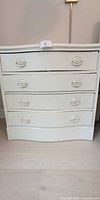 Front view showing four drawers, oval pulls, painted off-white finish, scalloped base