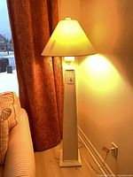 Full view of lit white pillar floor lamp beside sofa