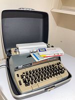 Typewriter seated in open hard case with paper loaded and envelopes on platen