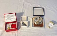 All four items laid out: boxed necklace, brooch, hummingbird compact, pill compact
