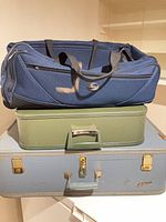 Stacked blue duffle, green suitcase, blue suitcase