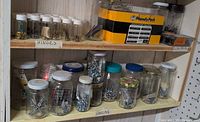 Shelf holding numerous glass jars, plastic vials and Handy Pack box filled with assorted nails, screws, anchors and other fasteners