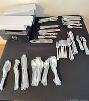 Overall view of bundled flatware sets on table, including boxed Oneida sets and loose grouped pieces