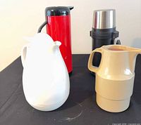 Four beverage containers: red thermos, black thermos, white carafe, beige carafe