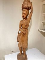 Full view of tall carved wooden female figure standing on round base
