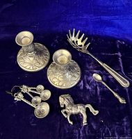 Group shot showing all items: two candleholders, four measuring spoons, pasta server, horse figurine, baby spoon