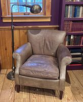 Front view of leather club chair beside brass floor lamp