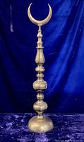 Full view of tall brass finial against blue backdrop