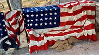 Two folded large U.S. 48-star flags draped over railing; cast iron eagle plaque below