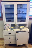 Front view of enameled metal kitchen cabinet with included ceramics, amber glass items and Celia Birtwell tin visible