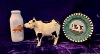 Group shot of milk bottle, cast iron cow bank, Warren Kimble tray on stand