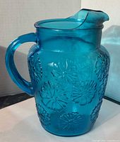 Front view of blue glass pitcher showing daisy pattern and spout