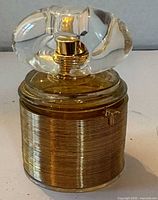 Fragrance bottle front view showing gold-tone sleeve and sculptural cap