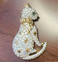 Front view of pavé rhinestone cat brooch showing gold bow and green eye