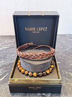 Bracelet set displayed in open Mario Lopez box: braided leather bracelet on top, tiger's eye bracelet below