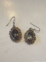 Front view of earrings showing iridescent stones and ornate silver frame