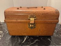 Front view of orange metal toolbox with brass latch and carry handle