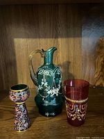 Three items: green enamel glass pitcher, cloisonné-style shot cup, ruby red enamel tumbler
