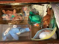 Drawer with brown bear, green frog, blue plush and other Beanie Babies in display boxes