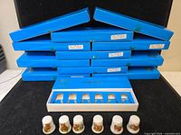 Stack of twelve blue boxes, one opened showing six thimble slots and six thimbles seated in front