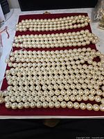 Ten strands of faux pearls laid flat on red surface