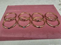 Eight gold-tone hinged bangles displayed on pink cloth