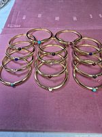 All twelve gold-tone bangles arranged in three rows on pink cloth