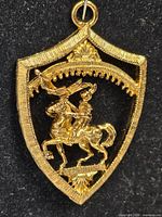 Front view of gold-tone shield pendant/brooch showing mounted warrior design