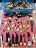Overview of wristwatches on cloth and additional straps and watches in blue bin