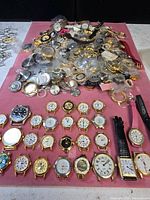 overview of entire lot showing wristwatches, bagged parts and straps on pink surface