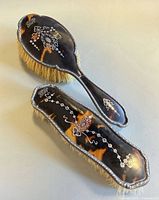 Top view of both brushes showing tortoiseshell backs and silver pique inlay