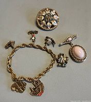 Group shot of four jewellery pieces: bar brooch with locket, charm bracelet, round brooch, oval cabochon brooch