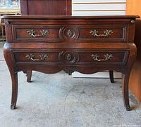 Front view of walnut chest showing serpentine drawers and brass hardware