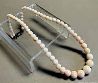 Full view of graduated coral bead necklace displayed on stand