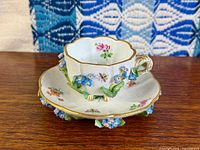 Cup on saucer showing applied flowers and painted motifs