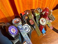 Group of approximately ten themed wristwatches on cushion