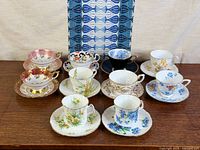 Ten assorted floral bone china teacup and saucer duos on wood surface