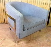 Front angled view of grey upholstered armchair with metal side panel