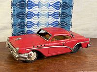 Left front three-quarter view of red tin Buick showing body details and wheel damage