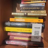 Box of books showing spines including Bleachers, Homeland, Little Bee, Resurrecting Midnight, Partner to History and others with MaxSold tag