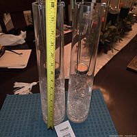Two tall crackle glass cylinder candle holders with tape measure showing height